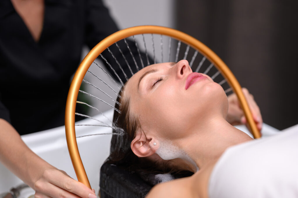 Woman enjoying a Japanese head spa treatment with a gold waterfall scalp rinse, promoting relaxation and scalp wellness.