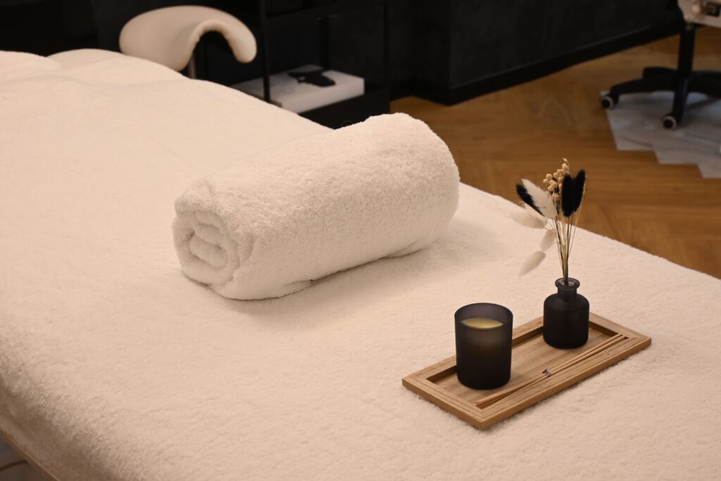 Luxury spa treatment bed with a rolled white towel, candle, and dried floral arrangement, creating a peaceful atmosphere for relaxation and wellness.